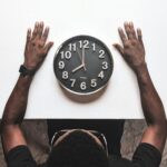 High angle view of a man with an apple watch observing a clock on a white table.