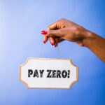 A hand holds a "Pay Zero!" sign against a vibrant blue backdrop, offering copyspace.