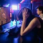 A young female gamer looks frustrated while playing on a computer in a neon-lit gaming room.